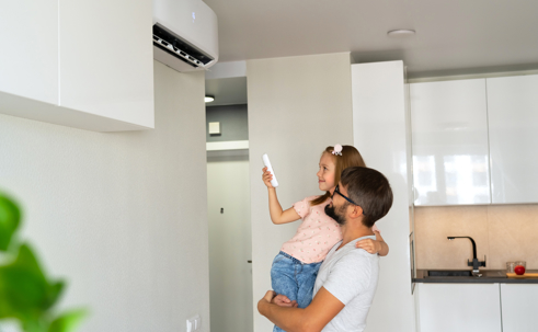 a father carrying his daughter who's adjusting the AC